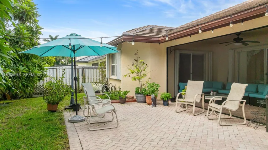 Covered patio with paver flooring, overhead ceiling fan, and string lighting, complemented by a dedicated exterior paver area