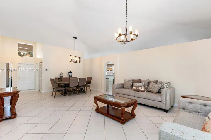 Vaulted ceilings, large-format tile flooring, arched wall pass-through, and dual tiered lighting fixtures
