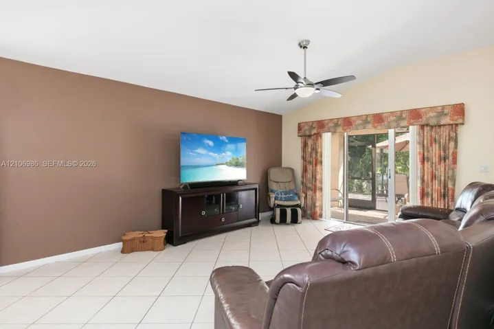 Living area with vaulted ceilings, neutral tile flooring, a stainless steel and glass ceiling fan, and sliding glass doors with exterior access