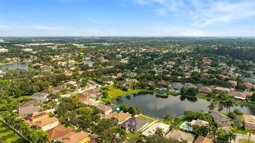 Aerial perspective of a property situated on a lakefront lot featuring a multi-pitched roofline, palm trees, and mature landscaping