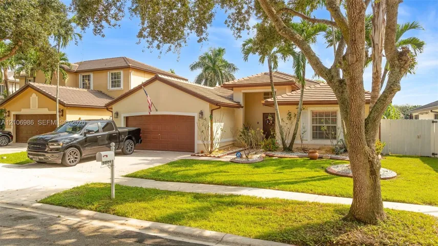 Stucco exterior residence featuring a multi-gable tile roof, attached two-car garage, and manicured front lawn with mature landscaping