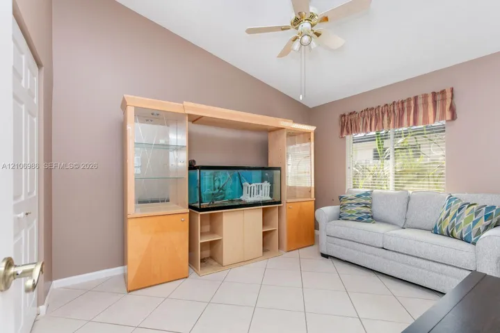 Room featuring vaulted ceilings, light-tone tile flooring, built-in wooden cabinetry with glass-paneled display shelving, and a ceiling fan
