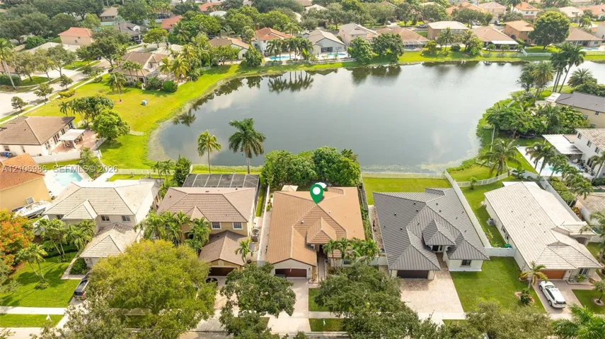 Aerial perspective of waterfront property featuring a multi-pitched shingle roof, paved driveway, attached garage, and landscaped grounds
