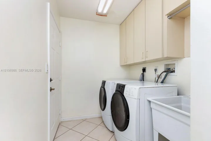 Laundry area featuring built-in upper cabinetry, utility sink, tile flooring, and overhead lighting