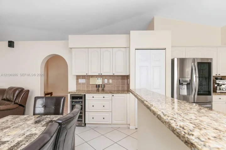 Kitchen featuring white cabinetry, stone-finish countertops, built-in wine cooler, stainless steel refrigerator, and arched doorway