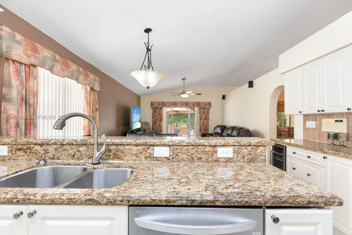 Kitchen featuring stone countertops, a dual-basin stainless steel sink with a high-arch faucet, white cabinetry, a built-in wine refrigerator, and decorative pendant lighting