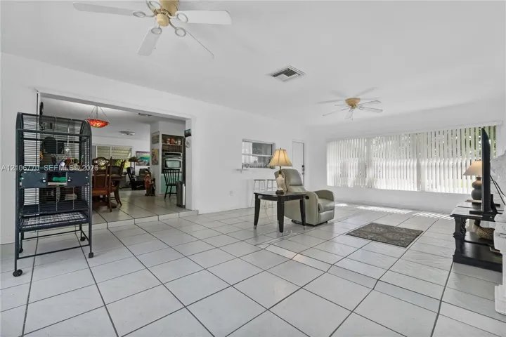 Living area featuring white ceramic tile flooring, dual ceiling fans, and large windows with vertical blinds