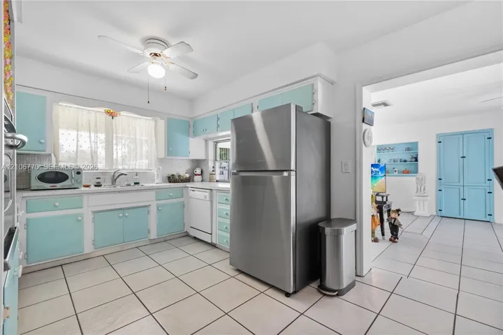 Kitchen featuring cabinetry with light blue finish, stainless steel refrigerator, white dishwasher, tile flooring, and ceiling fan with integrated lighting