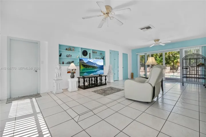 Living area featuring large-format tile flooring, built-in recessed shelving, dual ceiling fans, and a sliding glass door