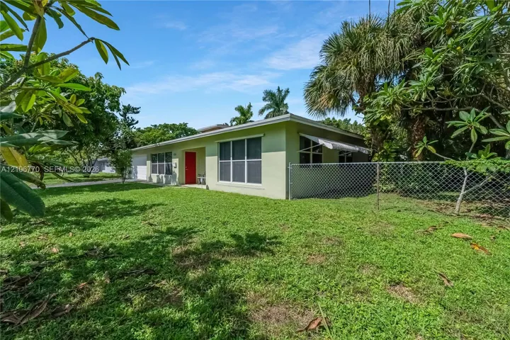 Single-story residence featuring light-colored stucco siding, a bold red entry door, large grid-pattern windows, and a chain-link fenced perimeter