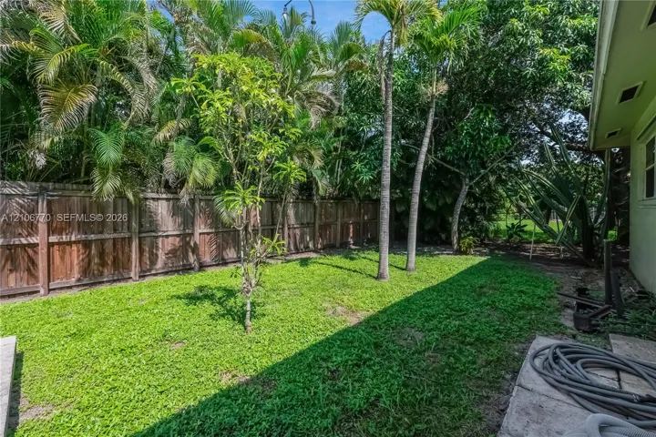 Backyard featuring a grass lawn, perimeter wood fencing, and mature palm trees