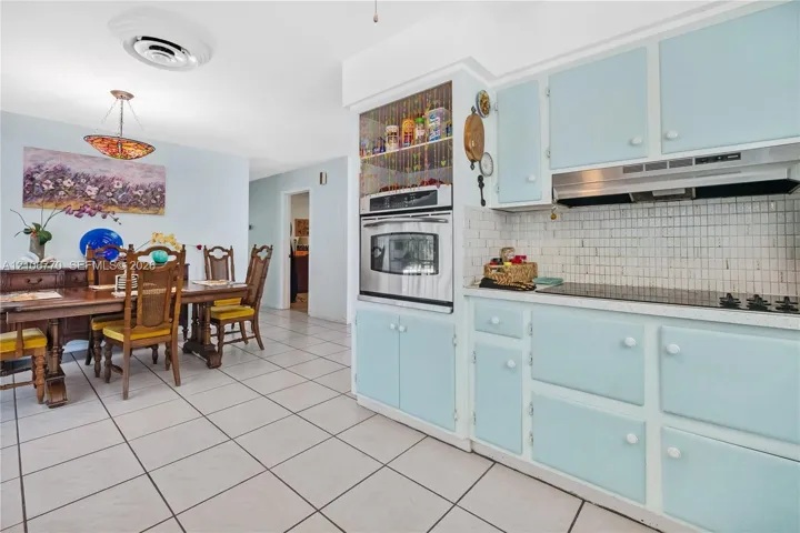 Kitchen featuring custom blue cabinetry, built-in stainless steel wall oven, ceramic tile backsplash, and ceramic tile flooring