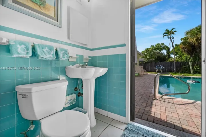 Ceramic tile wainscoting, white porcelain pedestal sink, and direct egress to a brick-paved pool deck