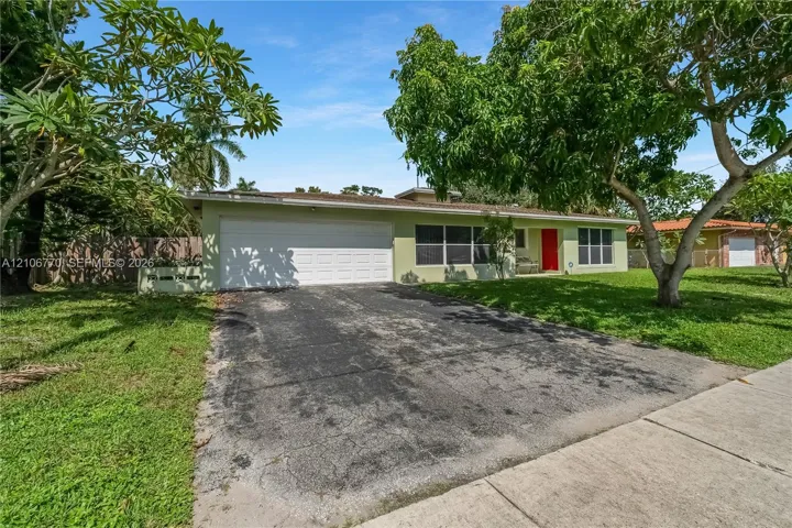 Single-story residence featuring a two-car garage, low-pitch roofline, and bright red front entry door set within a landscaped lot with mature trees