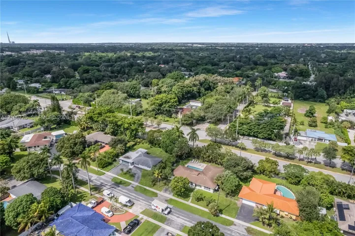 Aerial perspective of a residential neighborhood featuring mature canopy trees, varied housing styles, established paved streets, and residential swimming pools