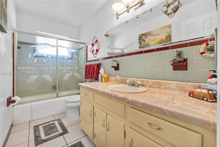 Bathroom featuring a stone-surface vanity with an integrated oval sink, ceramic tile wainscoting, a wall-to-wall mirror, and a tub-shower combination with sliding etched glass doors