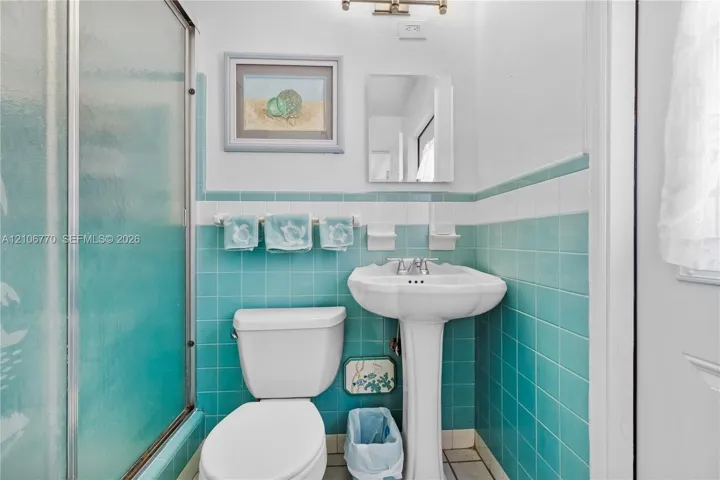 Bathroom featuring teal wall tiling with white accent trim, a white pedestal sink, a glass-enclosed shower, and built-in ceramic soap dishes