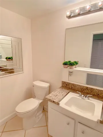 Bathroom featuring a vanity with a stone-finish countertop, undermount sink, multi-bulb overhead lighting, oversized wall mirror, and neutral tile flooring