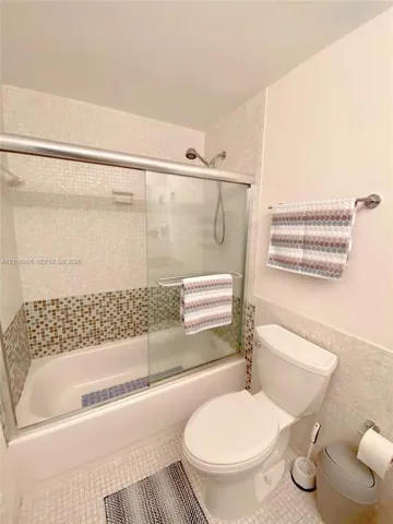 Bathroom featuring a shower-tub combination with sliding glass doors, multi-toned mosaic tile accents, and a wall-mounted hand-held shower head