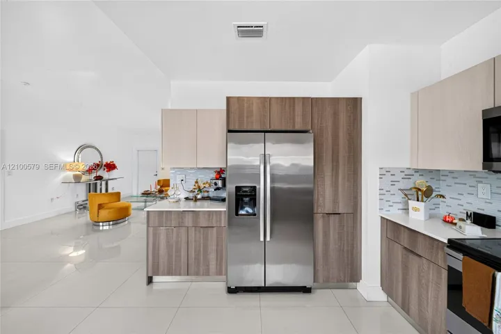 Kitchen featuring two-tone cabinetry, stone countertops, tiled backsplash, stainless steel appliances, and large-format flooring