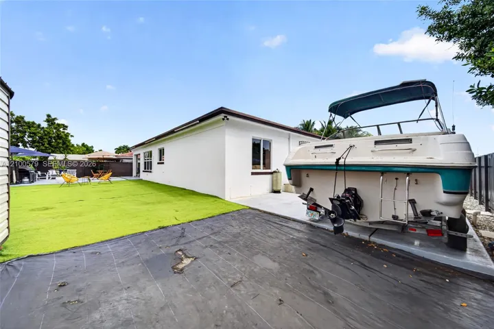 Rear exterior space featuring a white stucco facade, a concrete slab, and a green lawn area