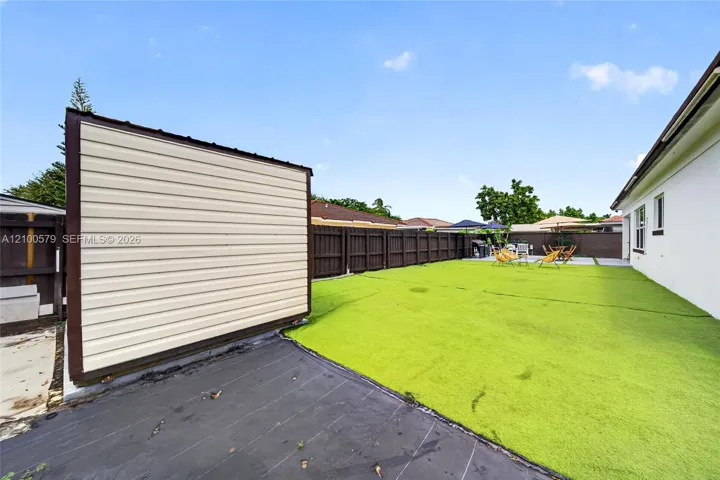 Fenced backyard featuring synthetic turf, a standalone storage structure with horizontal siding, and a paved concrete patio area