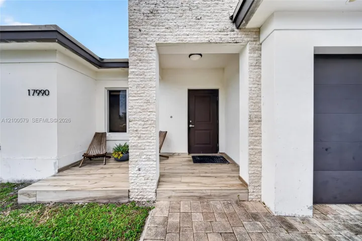 Exterior facade featuring a stone-veneer entryway, wood-finish flooring on the porch, a modern dark-toned front door, and a paver walkway