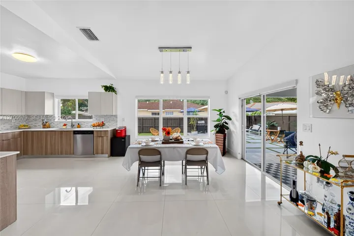 Open-concept living space featuring high-gloss tile flooring, cabinetry with wood-finish base and light upper units, mosaic tile backsplash, stainless steel dishwasher, and sliding glass doors