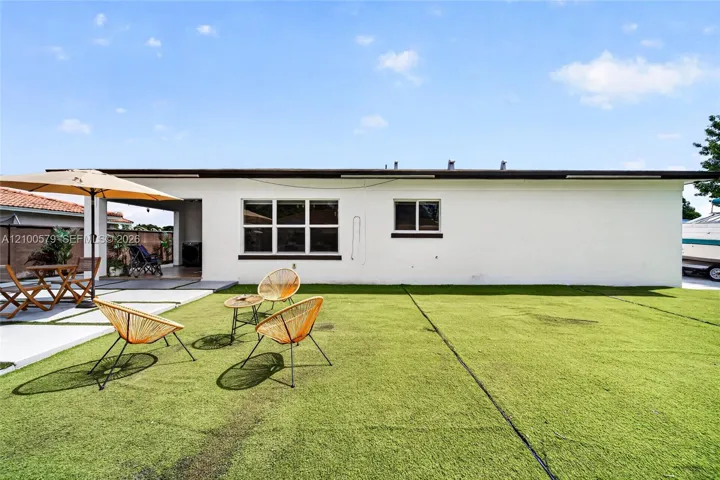 Backyard featuring a covered patio, concrete hardscaping, and synthetic turf lawn