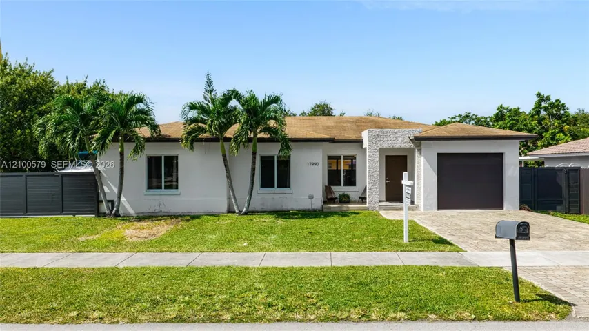 Single-story residence featuring a smooth stucco exterior, decorative stone facade accent, paved driveway, integrated garage, and privacy fencing
