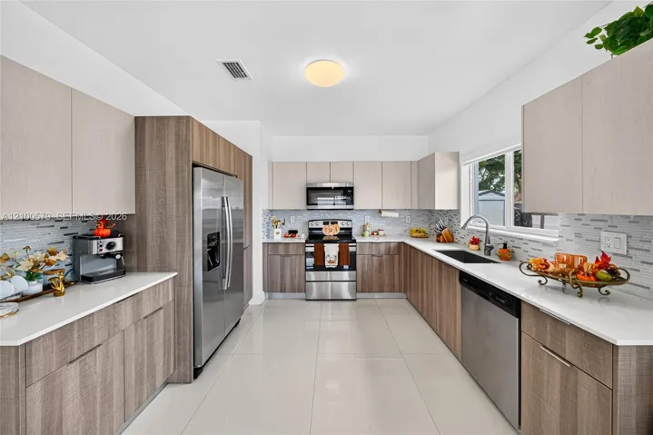 Kitchen featuring dual-tone cabinetry, stainless steel appliances, white solid-surface countertops, tile backsplash, and light-colored tile flooring