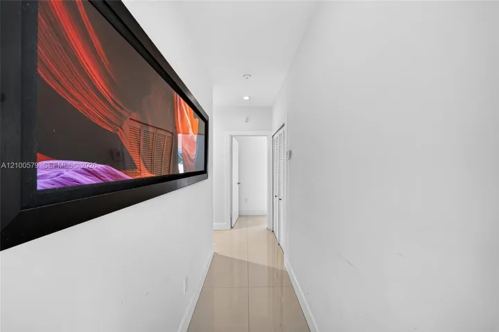 Hallway featuring neutral-toned tile flooring, recessed ceiling lighting, and louvered closet doors