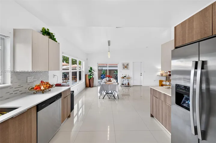 Kitchen featuring flat-panel wood-finish cabinetry, white countertops, stainless steel appliances, tile backsplash, and polished tile flooring