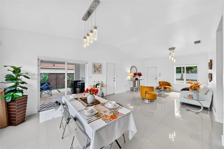 Open-concept interior featuring large-format tile flooring, recessed lighting, polished multi-light pendant fixtures, and sliding glass doors leading to a covered patio