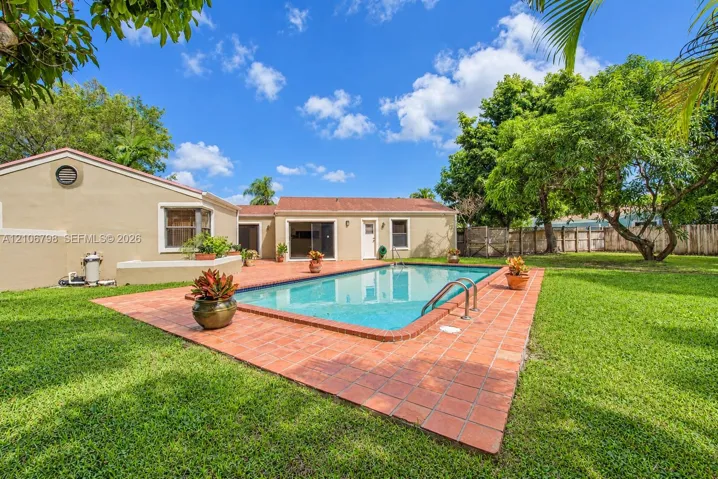 Rear exterior featuring an in-ground swimming pool, tile patio surround, expansive lawn, and mature landscaping