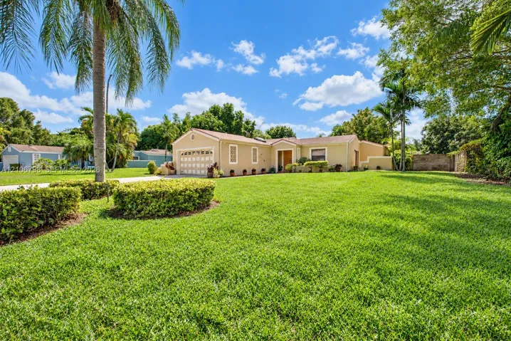 Single-story residence featuring a stucco exterior, multi-car garage, mature tropical landscaping, and an expansive lawn