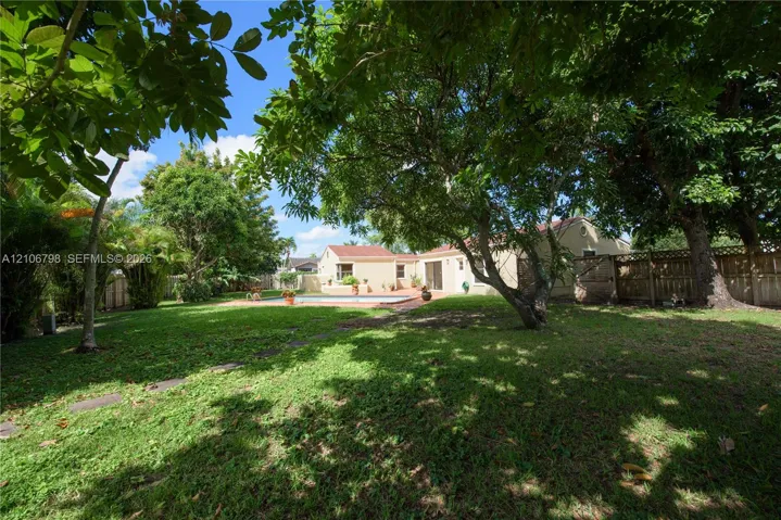 Expansive backyard featuring a large swimming pool, paved patio, mature shade trees, and a wooden perimeter fence