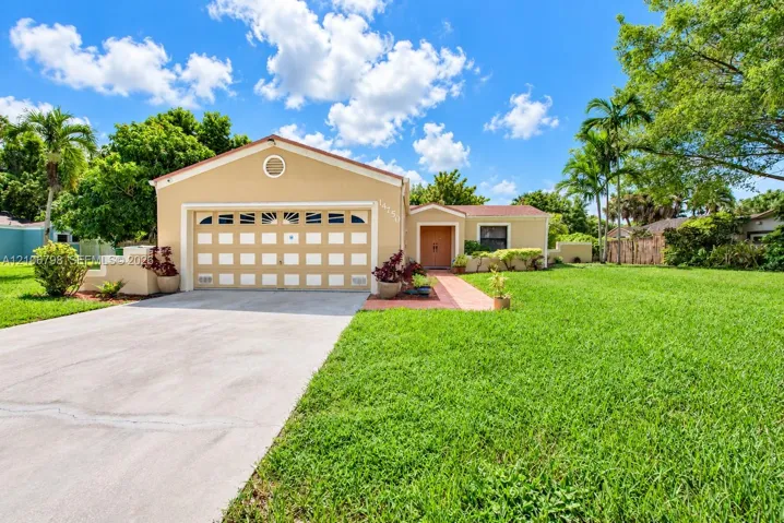 Stucco exterior featuring a two-car garage with arched decorative windows, concrete driveway, tiled entryway path, and expansive manicured lawn