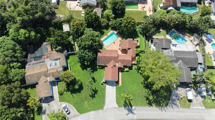 Aerial perspective of residential property featuring a multi-pitched roofline, a backyard swimming pool, paved driveway, and mature landscaping
