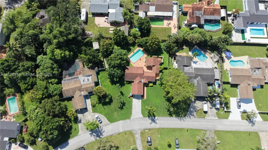 Aerial perspective of a property featuring a private swimming pool, terracotta-tiled patio, paved driveway, expansive lawn, and mature trees
