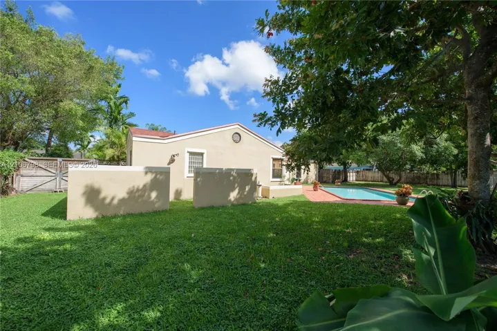Expansive backyard featuring a manicured lawn, inground swimming pool, paved patio, perimeter wood fencing, and mature trees
