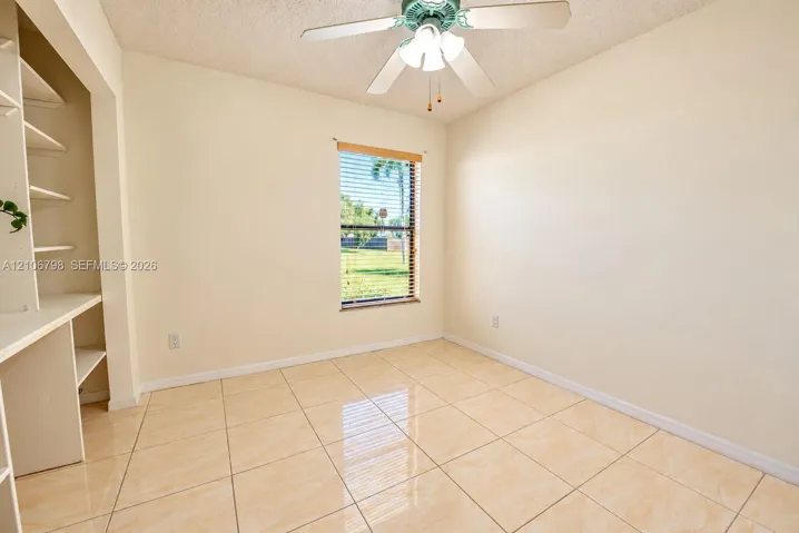 Room featuring large-format ceramic tile flooring, built-in shelving with an integrated desk, and a ceiling fan with integrated lighting