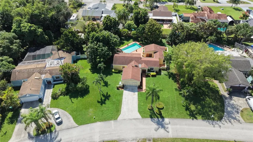 Aerial perspective of a sprawling corner lot featuring a multi-gable roofline, an attached multi-car garage, paved driveway, and an in-ground swimming pool