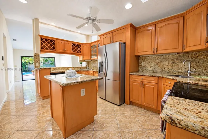 Kitchen featuring wood cabinetry, stone countertops, a central island, stainless steel refrigerator, and recessed lighting