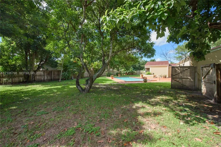 Expansive backyard featuring mature shade trees, a perimeter wood fence, in-ground swimming pool, and a brick-paver patio area
