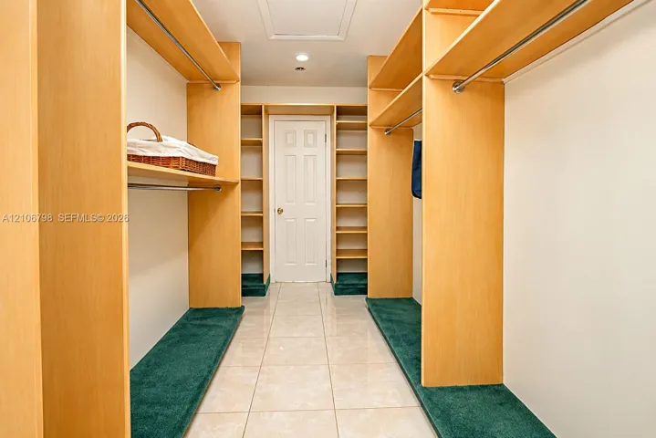 Walk-in closet featuring custom light wood-finish shelving, integrated hanging rods, wall-to-wall carpeting on storage tiers, and tile flooring
