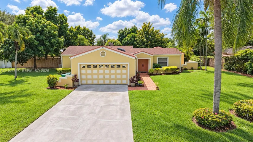 Single-story residence featuring a shingled roof, arched garage detailing, brick walkway, and extensive lawn landscaping with mature palms