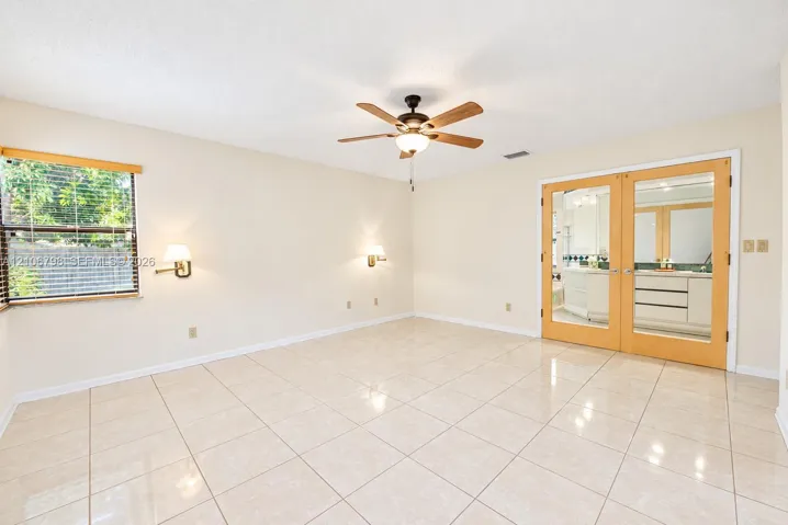 Neutral tile flooring, ceiling fan with light fixture, twin wall-mounted sconces, and wood-framed glass-paneled double doors