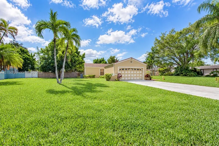 Single-story residence featuring a concrete driveway, multi-panel garage door, manicured lawn, and mature palm trees