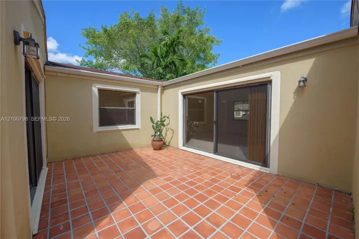 Private courtyard featuring terra-cotta tile flooring, stucco exterior walls, and two sets of sliding glass doors